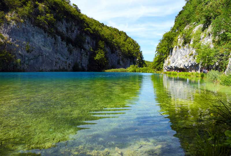 Ein glasklarer See liegt zwischen Wäldern und Felsen in Kroatien