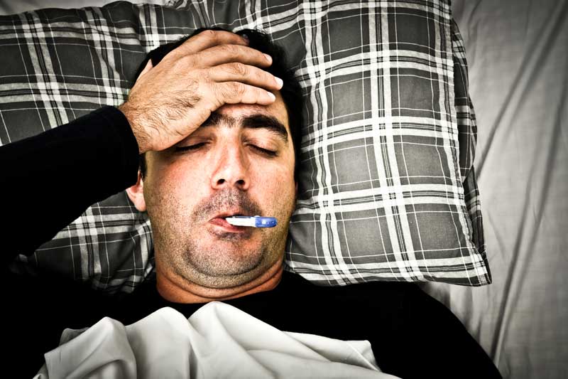 Ein Mann liegt krank mit Fieberthermometer im Bett