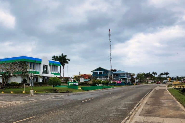 Eine ruhige Straße in Belmopan mit modernen Gebäuden, Palmen und bewölktem Himmel schafft eine friedliche Kleinstadtatmosphäre.