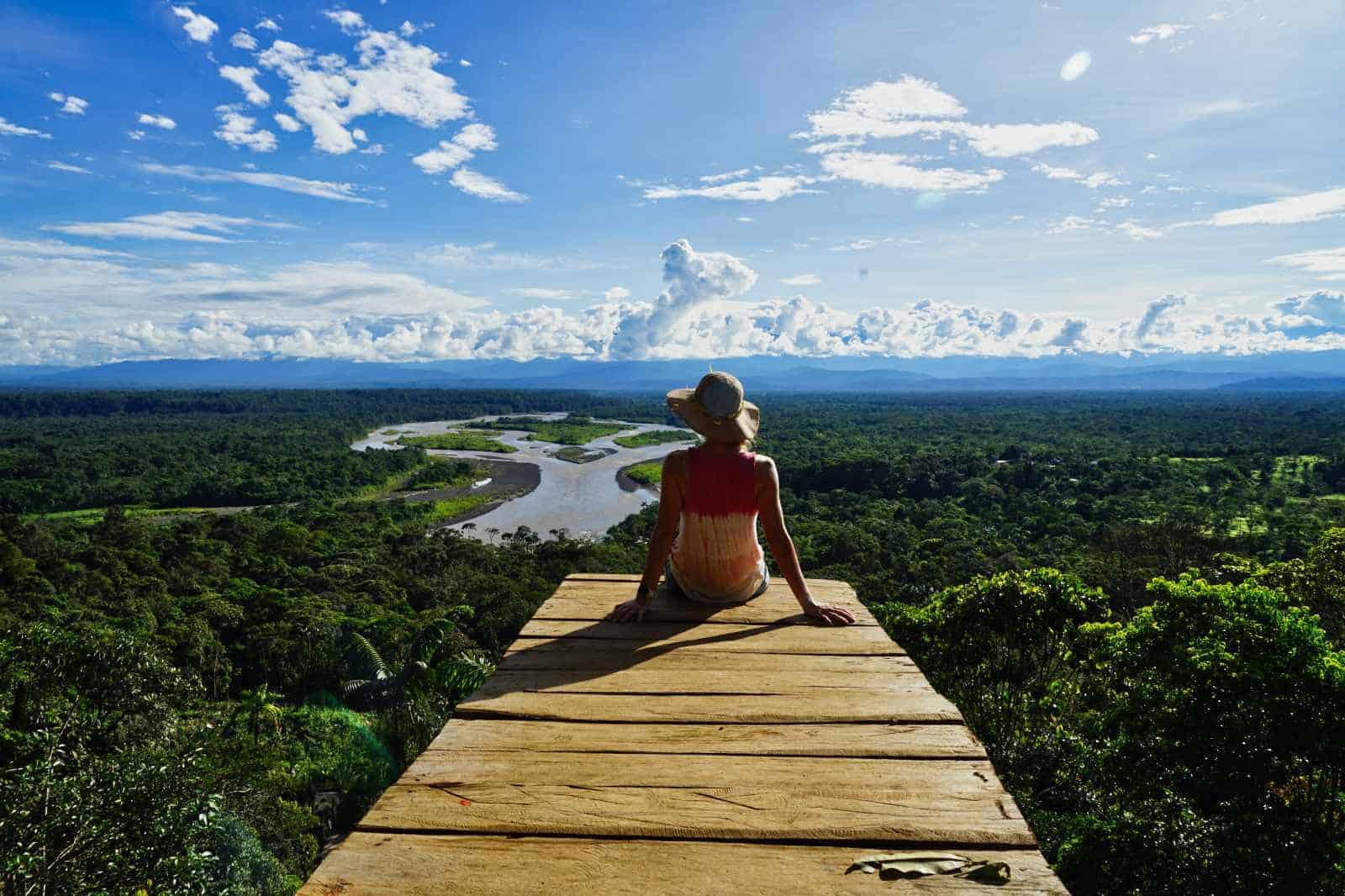 Eine Frau sitzt auf einem Steg mit gigantischem Ausblick über einen Fluss im Regenwald von Ecuador