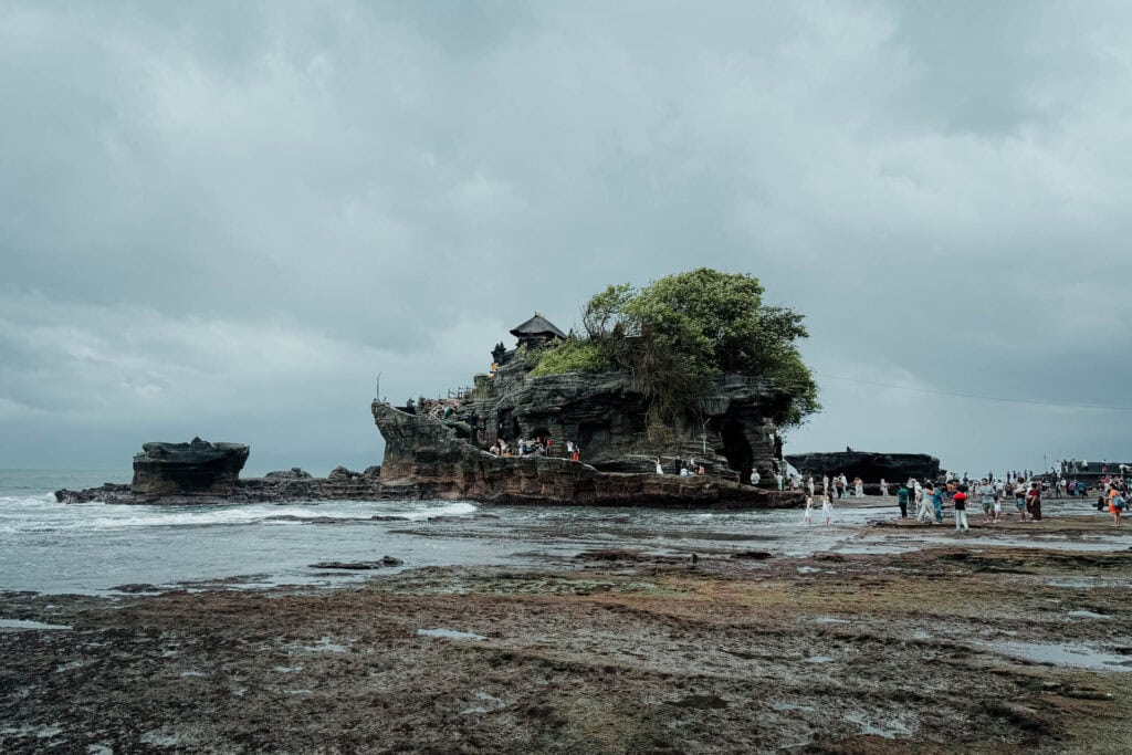 Unter einem wolkenverhangenen Himmel besuchen viele Menschen Tanah Lot, den ikonischen Tempel an der felsigen Küste von Bali.