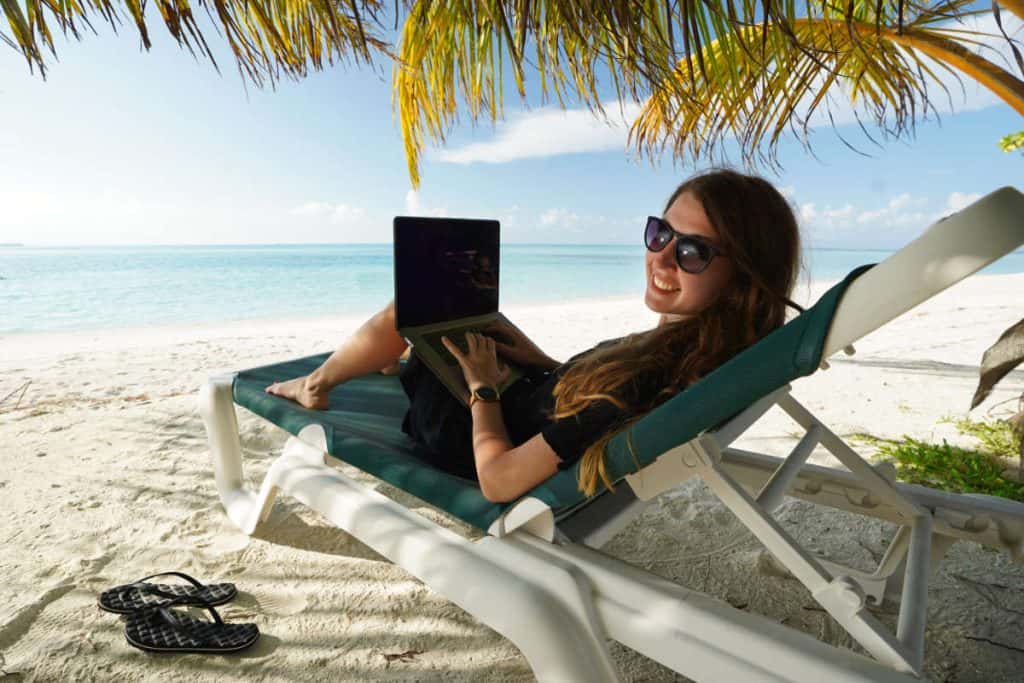 Digital Nomade Frau arbeitet mit Laptop am Strand
