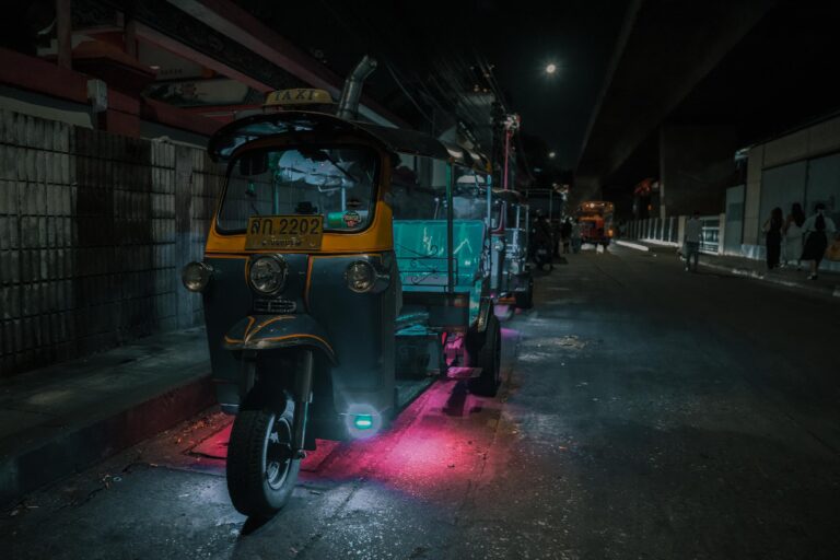 Ein Tuk-Tuk-Taxi mit Neonlichtern, das nachts auf einer schwach beleuchteten Straße geparkt ist - einer der lebhaften Fotospots, die Bangkok zu bieten hat.