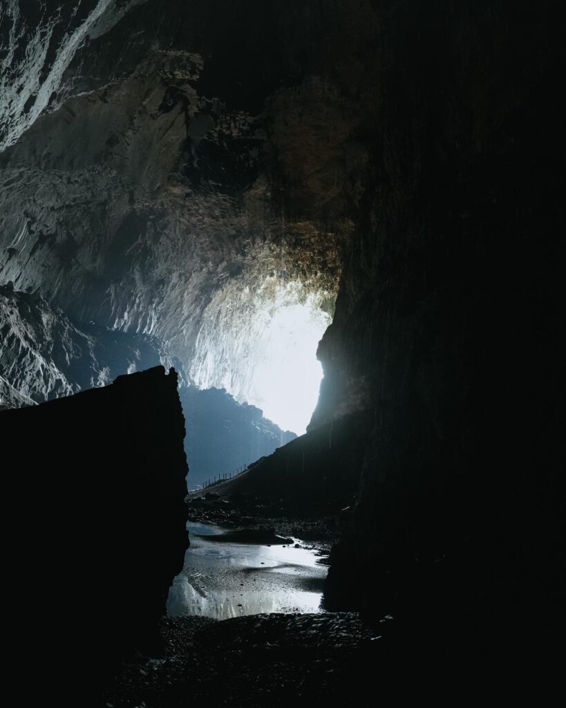 Eine dunkle Höhle, durch deren Eingang Sonnenlicht strömt und einen hellen Kontrast zum felsigen Inneren bildet.