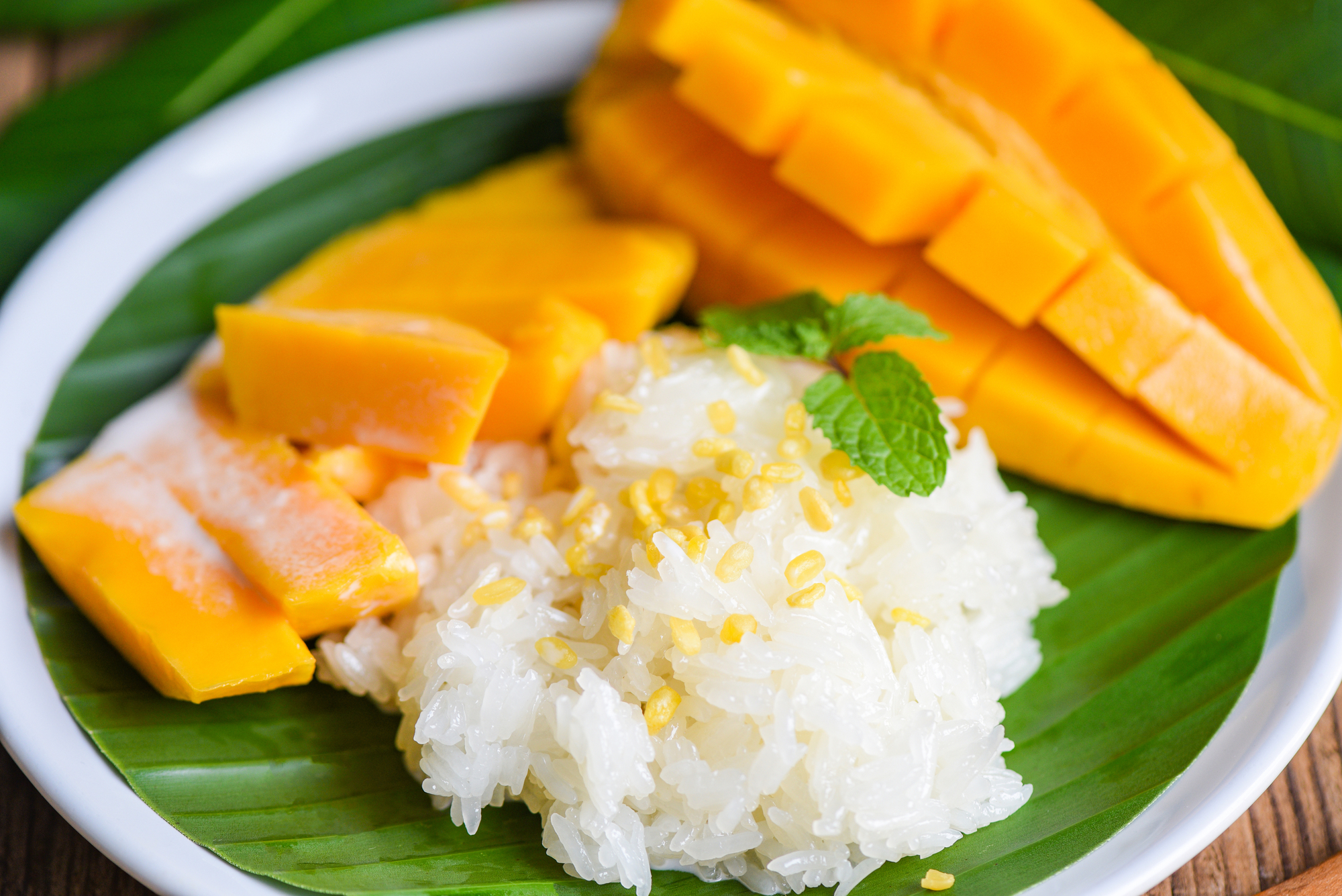 Ein Teller Mango-Klebreis mit Mangoscheiben und einem Minzblatt auf einem Bananenblatt.