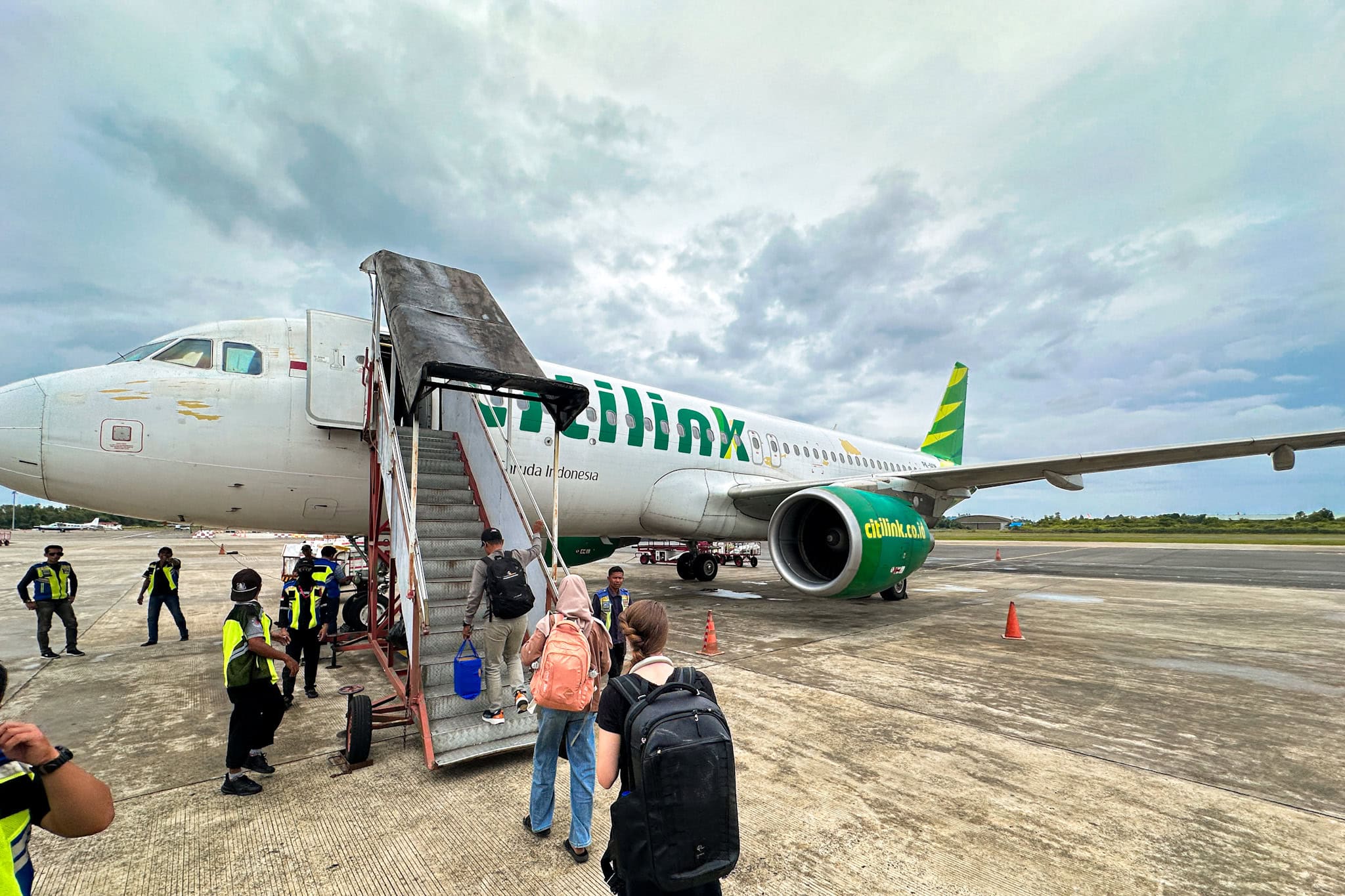 An einem bewölkten Tag besteigen Passagiere ein Citilink-Flugzeug über eine Treppe am Flughafen.