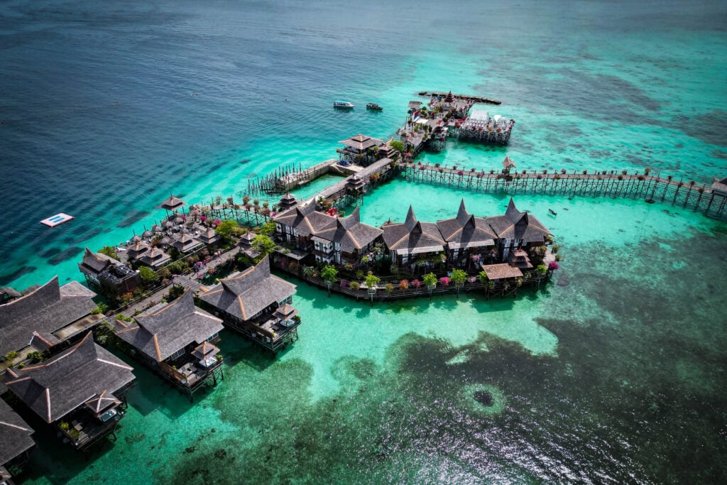 Luftaufnahme von Überwasserbungalows und Wegen am türkisfarbenen Meer in einem tropischen Resort.