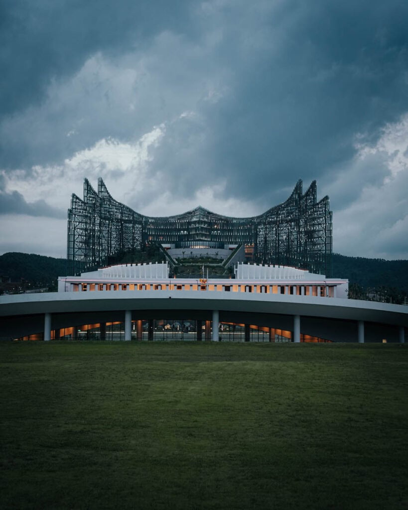 Modernes Gebäude mit geschichtetem Design vor einem wolkigen Himmel, umgeben von üppigem Grün und einem großen Rasen, der an die ruhigen Landschaften von Nusantara erinnert.