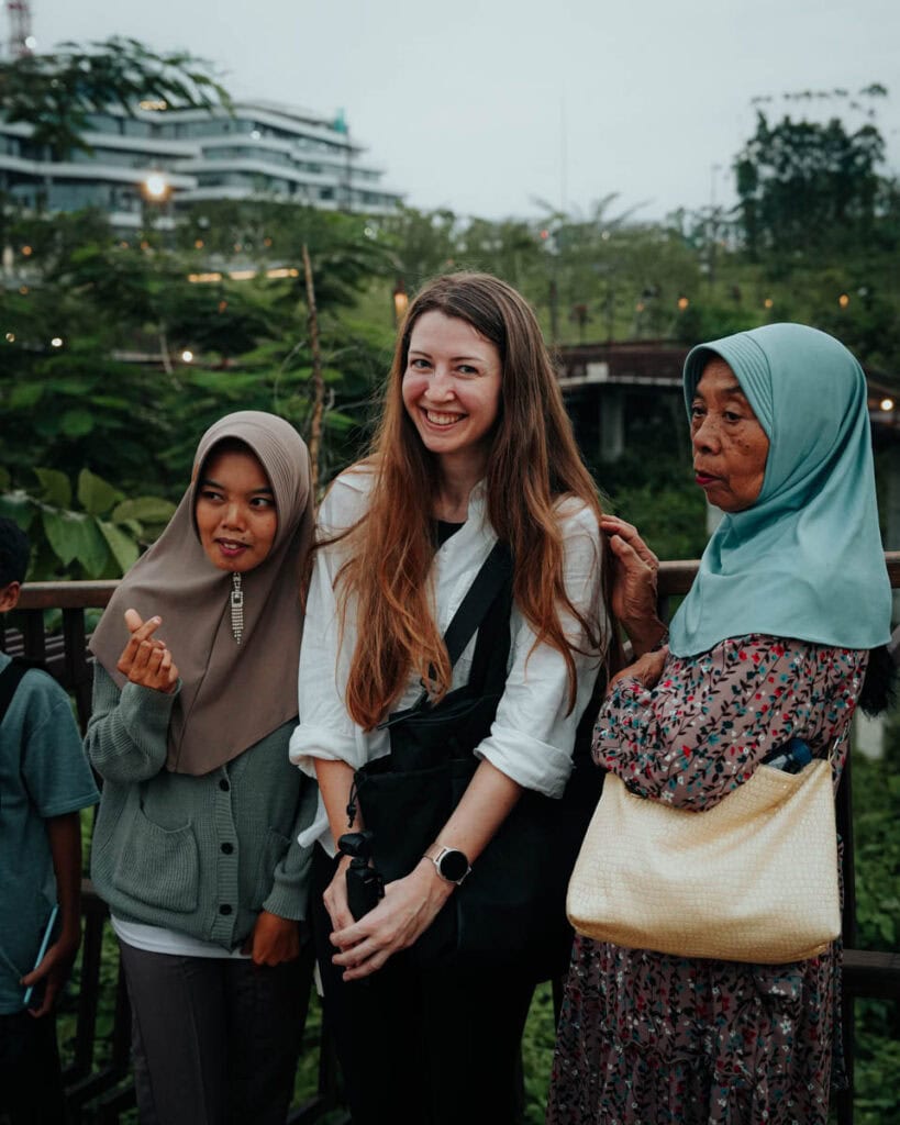 Drei Frauen stehen zusammen draußen, mit dem üppigen Grün und den traditionellen Gebäuden von Nusantara im Hintergrund.