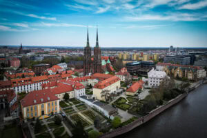 Luftaufnahme einer Stadt mit einer Kathedrale mit zwei Türmen, Gebäuden mit roten Dächern und einem Fluss auf der rechten Seite.