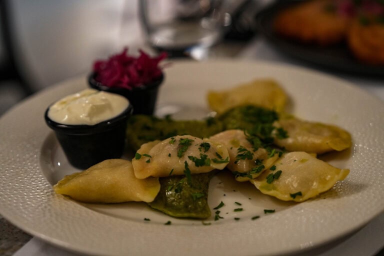 Ein Teller Pierogi mit zwei Dip-Saucen, garniert mit Kräutern, auf einem weißen Teller.