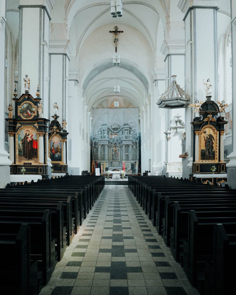 Innenraum einer großen Kirche mit Kirchenbänken, gewölbter Decke und reich verzierten Altären auf beiden Seiten.