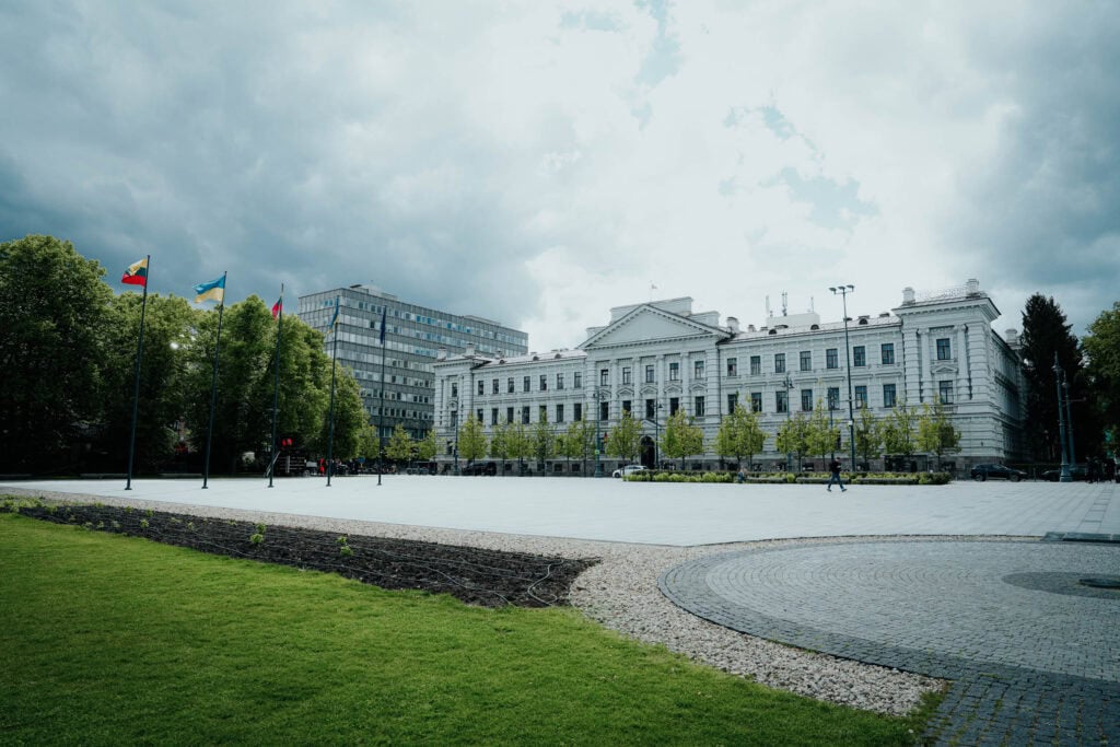 Ein großes, weißes neoklassizistisches Gebäude mit Flaggen und einem geräumigen Innenhof unter einem bewölkten Himmel.