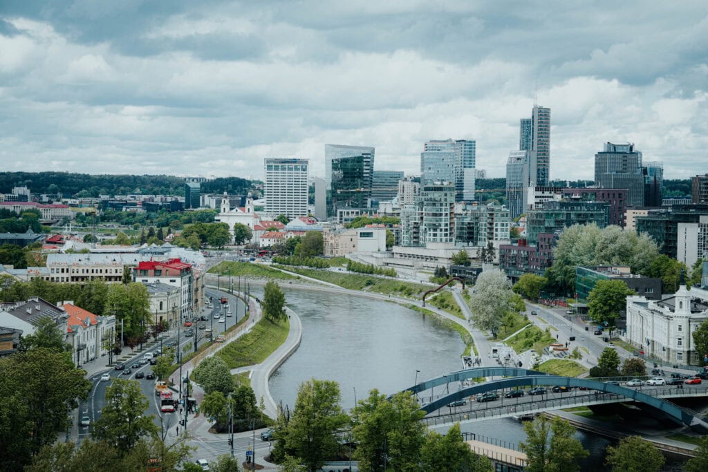 Eine Stadtlandschaft mit modernen Gebäuden, einem Fluss und einer geschwungenen Brücke unter einem bewölkten Himmel.