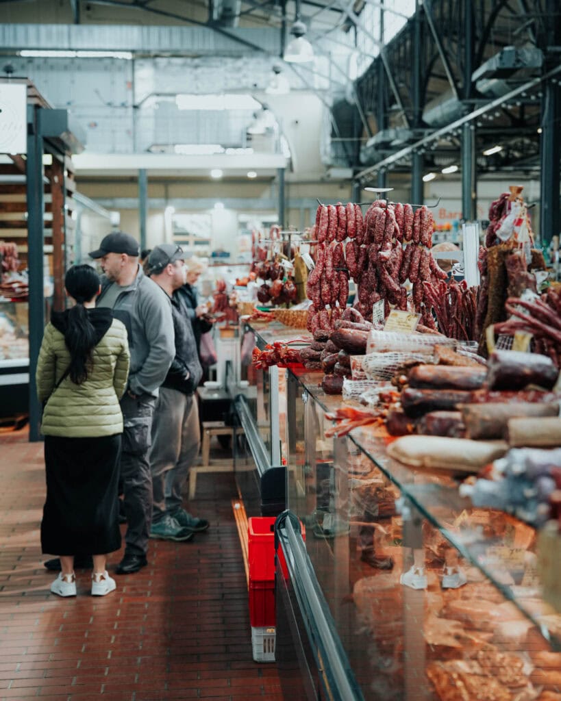 Menschen kaufen an der Feinkosttheke eines Marktes ein, wo verschiedene Wurst- und Fleischsorten ausgestellt sind.