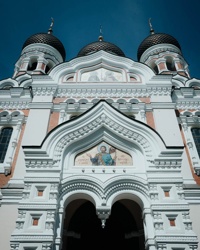 Weiße, reich verzierte russisch-orthodoxe Kirche mit Kuppeln und religiösen Ikonen, aus einem niedrigen Winkel vor dem blauen Himmel in Tallinn gesehen.