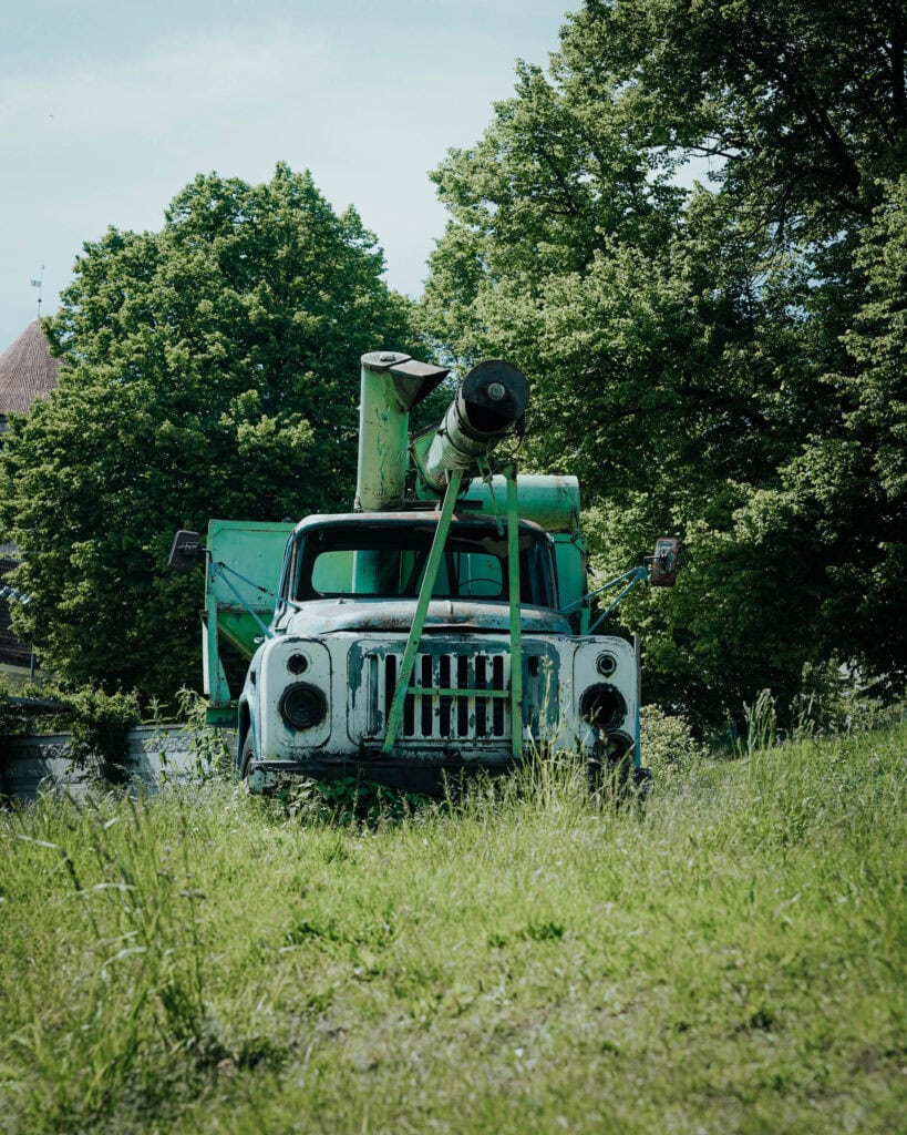 Altes, verwittertes Militärfahrzeug mit einer Kanone, geparkt im hohen Gras in der Nähe von Tallinn, mit Bäumen im Hintergrund.