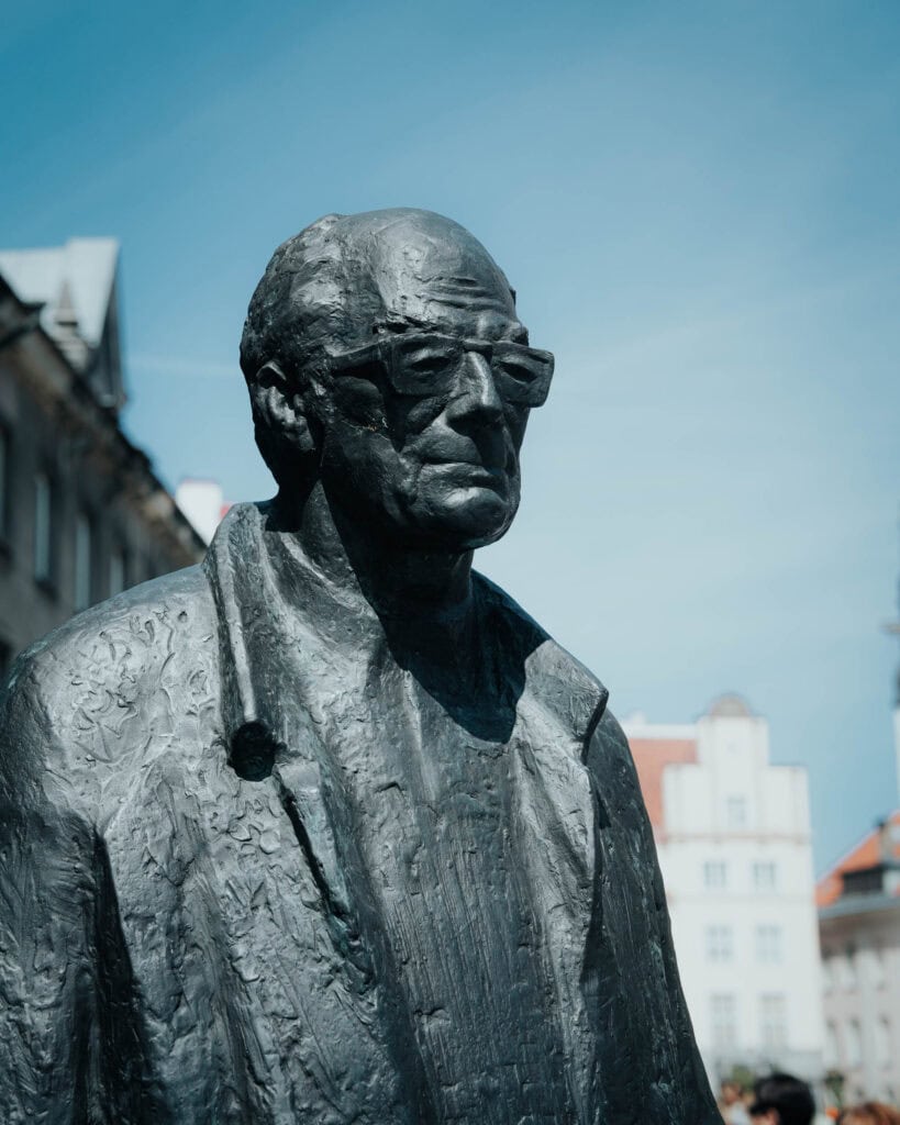 Bronzestatue eines Mannes mit Brille und Mantel, im Freien vor einem klaren blauen Himmel in Tallinn.