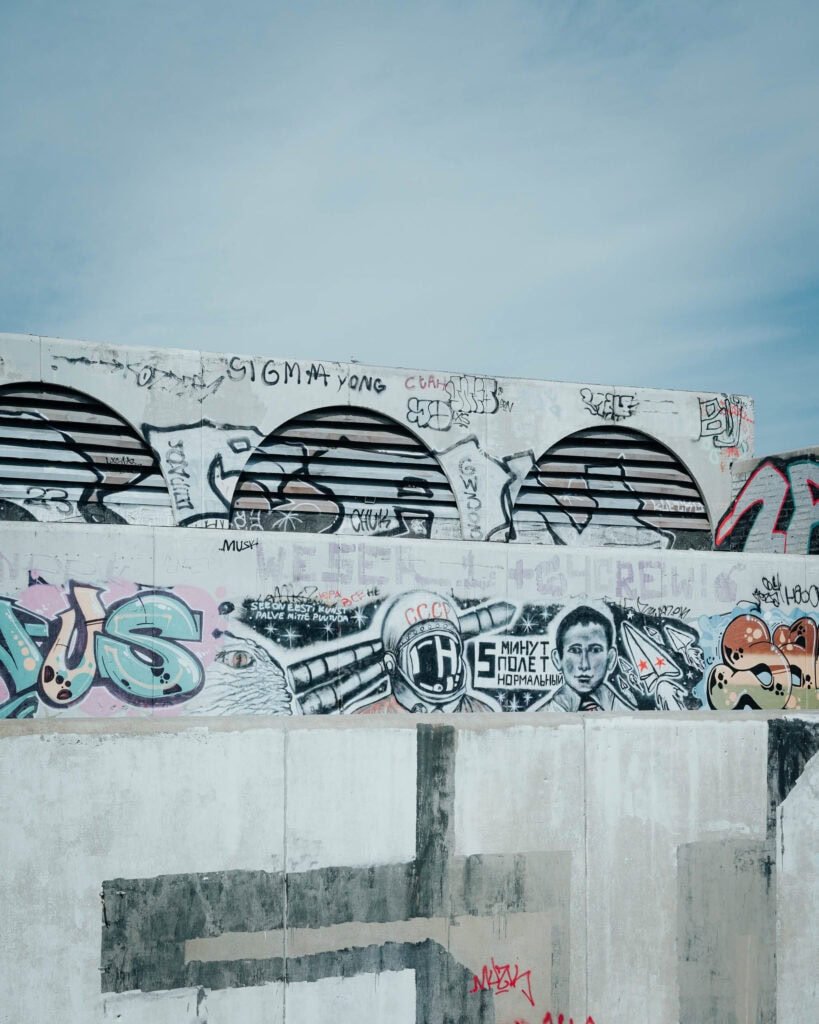 Eine Betonmauer mit bunten Graffiti und Wandmalereien erhellt die Straßen von Tallinn unter einem blauen Himmel.