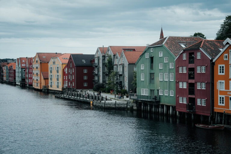 Bunte Holzhäuser auf Stelzen säumen die Uferpromenade unter einem bewölkten Himmel.