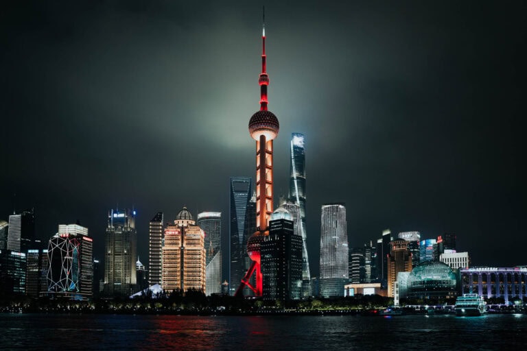 Die nächtliche Skyline von Shanghai mit dem Oriental Pearl Tower und beleuchteten Wolkenkratzern, die sich auf dem Wasser spiegeln.