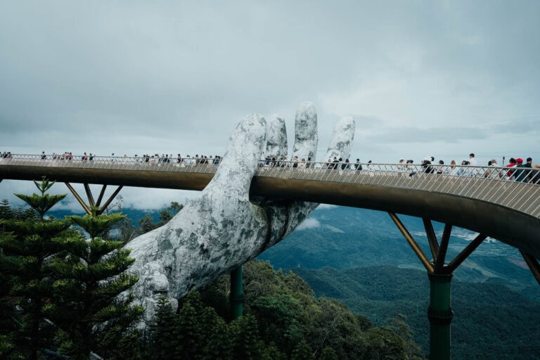 Die Goldene Brücke in Vietnam, die von riesigen steinernen Händen gehalten wird, ist überfüllt mit Besuchern und bietet einen Blick auf üppig grüne Berge.