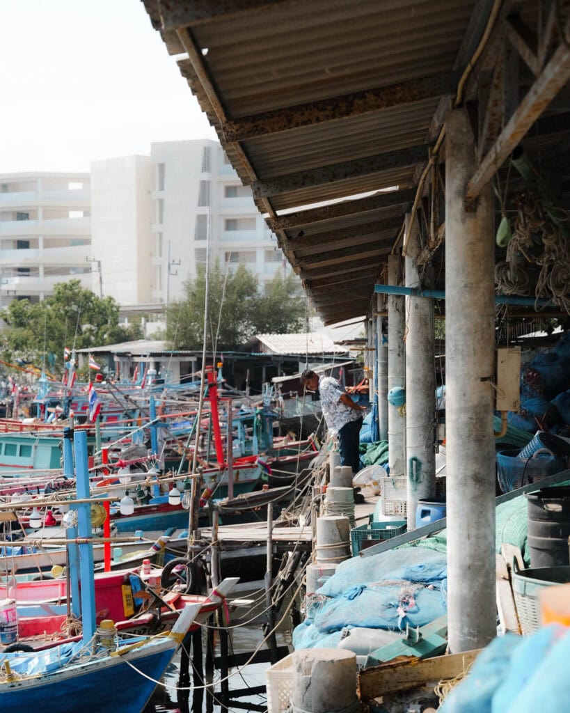 Bunte Fischerboote, die an einem belebten Hafen angedockt sind, mit Gebäuden und einer Person, die auf dem Pier arbeitet.
