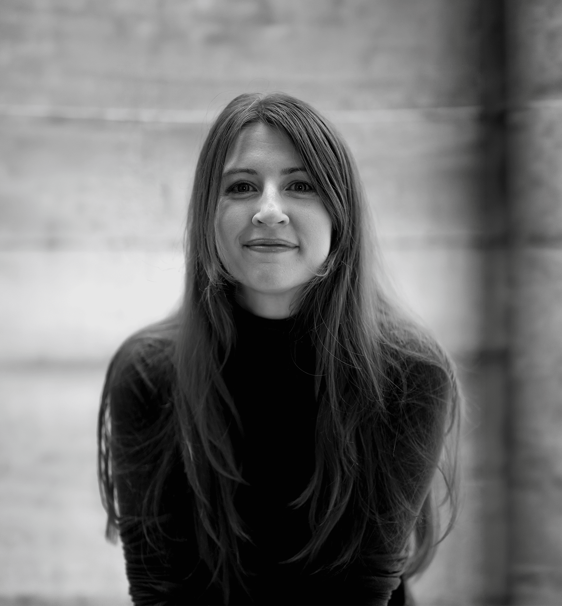 Die Autorin Martina B. Fruth in einem dunklen Oberteil, lächelnd, sitzt vor einem unscharfen Steinhintergrund. Schwarz-Weiß.