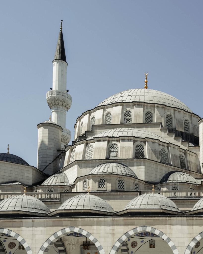Eine große Moschee mit einer zentralen Kuppel, einem Minarett und Bogenfenstern unter einem strahlend blauen Himmel.