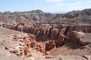 Ein Canyon aus rotem Fels mit geschichteten Klippen und zerklüftetem Gelände unter einem blauen Himmel mit vereinzelten Wolken.