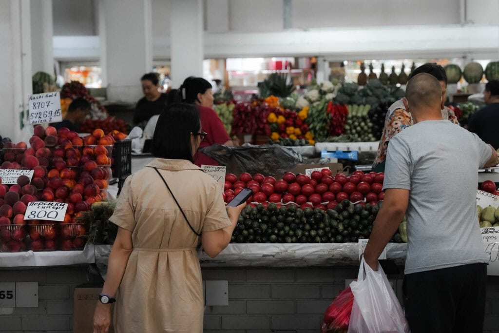 Menschen, die auf einem Hallenmarkt mit farbenfrohen Auslagen frisches Obst und Gemüse einkaufen.