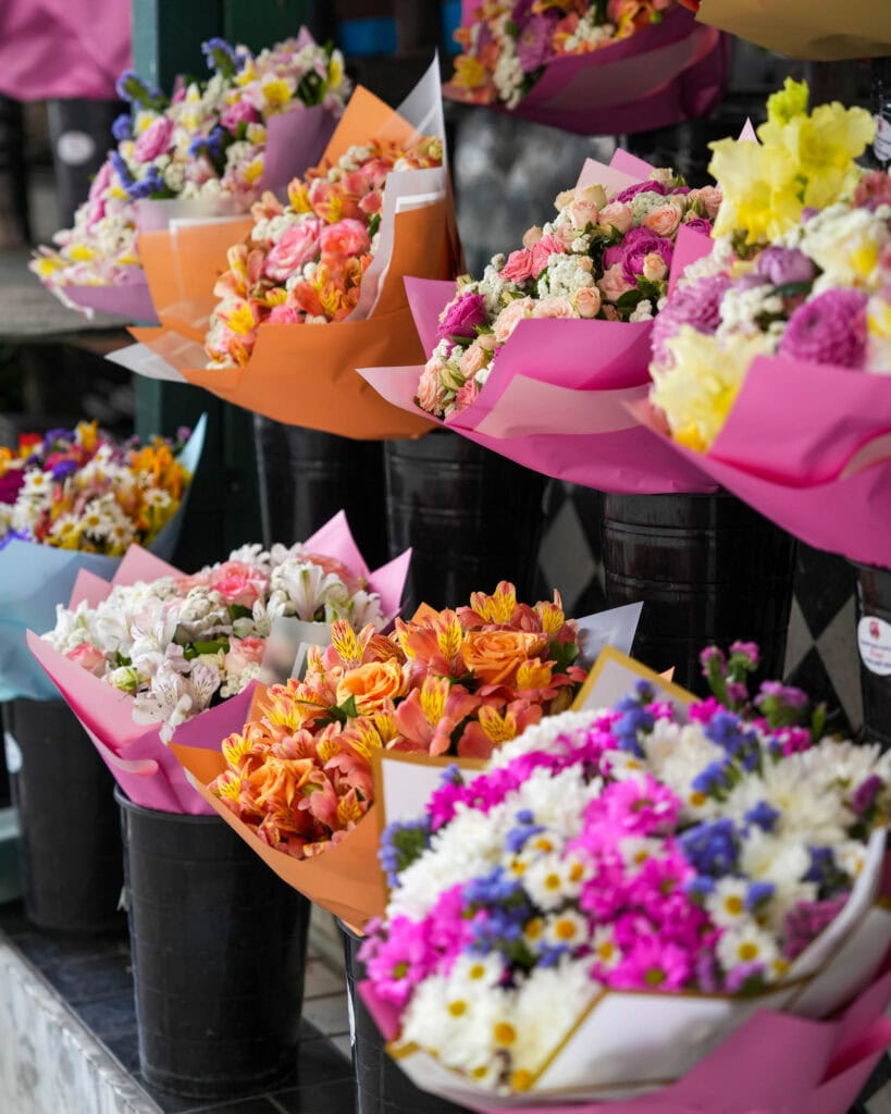 Bunte Blumensträuße aus verschiedenen Blumen, in Papier eingewickelt, die auf einem Markt in schwarzen Eimern ausgestellt sind.
