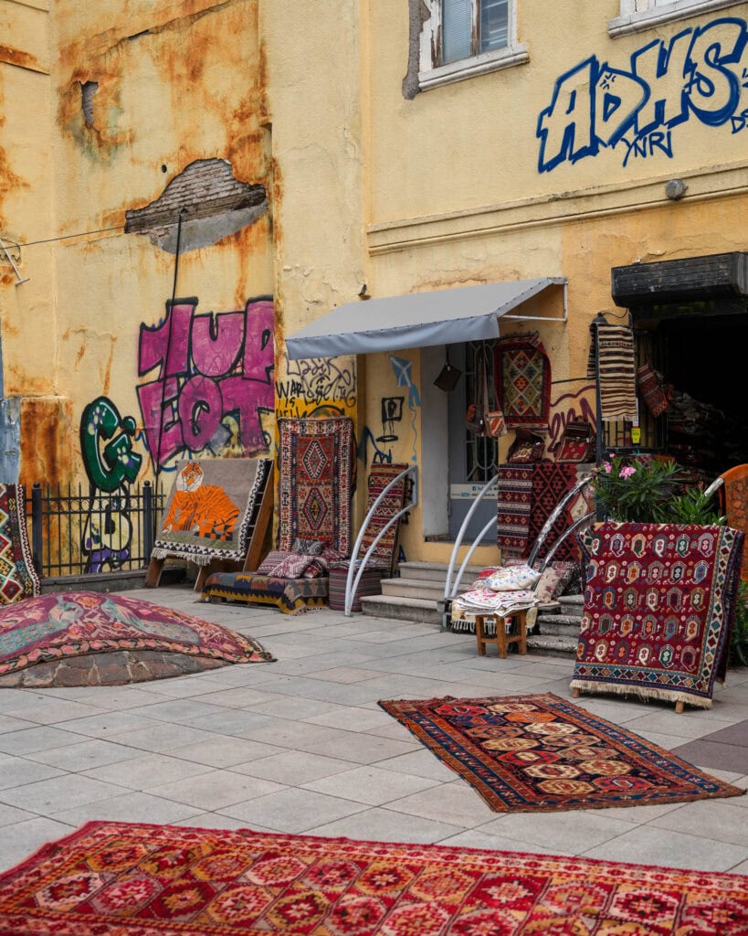 Bunte Teppiche, ausgestellt vor einem Laden mit gelben, mit Graffiti übersäten Wänden und abblätternder Farbe.