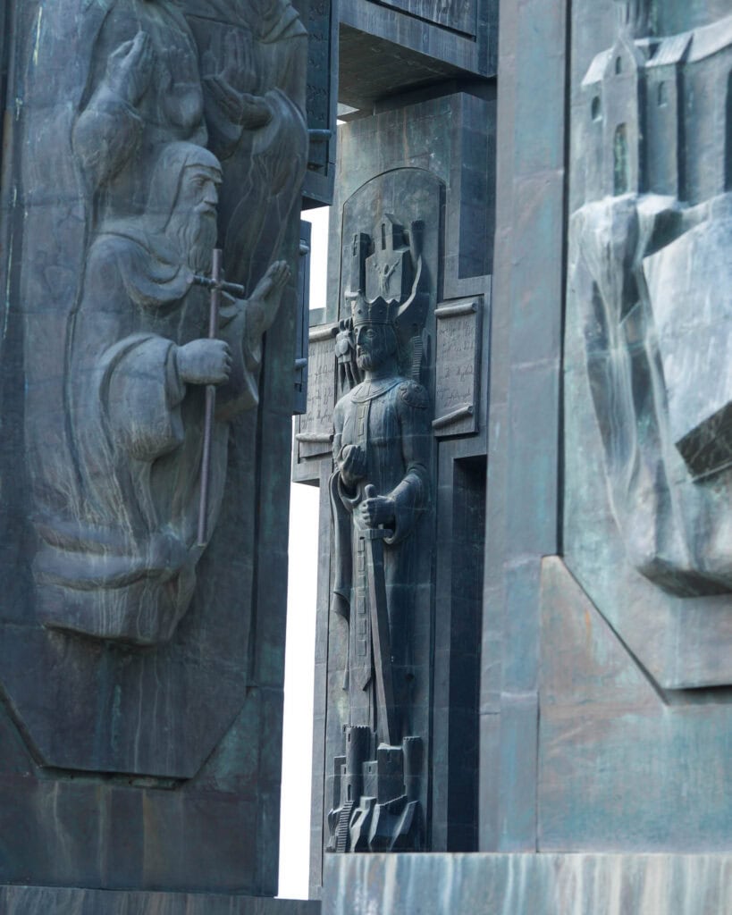 Große, detailreiche Steinstatuen, die historische Persönlichkeiten darstellen – eine davon hält ein Kreuz in der Hand –, auf einem monumentalen Bauwerk.