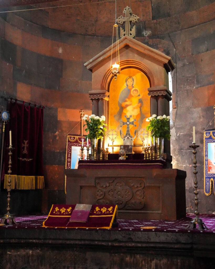 Altar mit Kerzen, Blumen und einem Gemälde der Madonna mit Kind in einer Steinkirche.