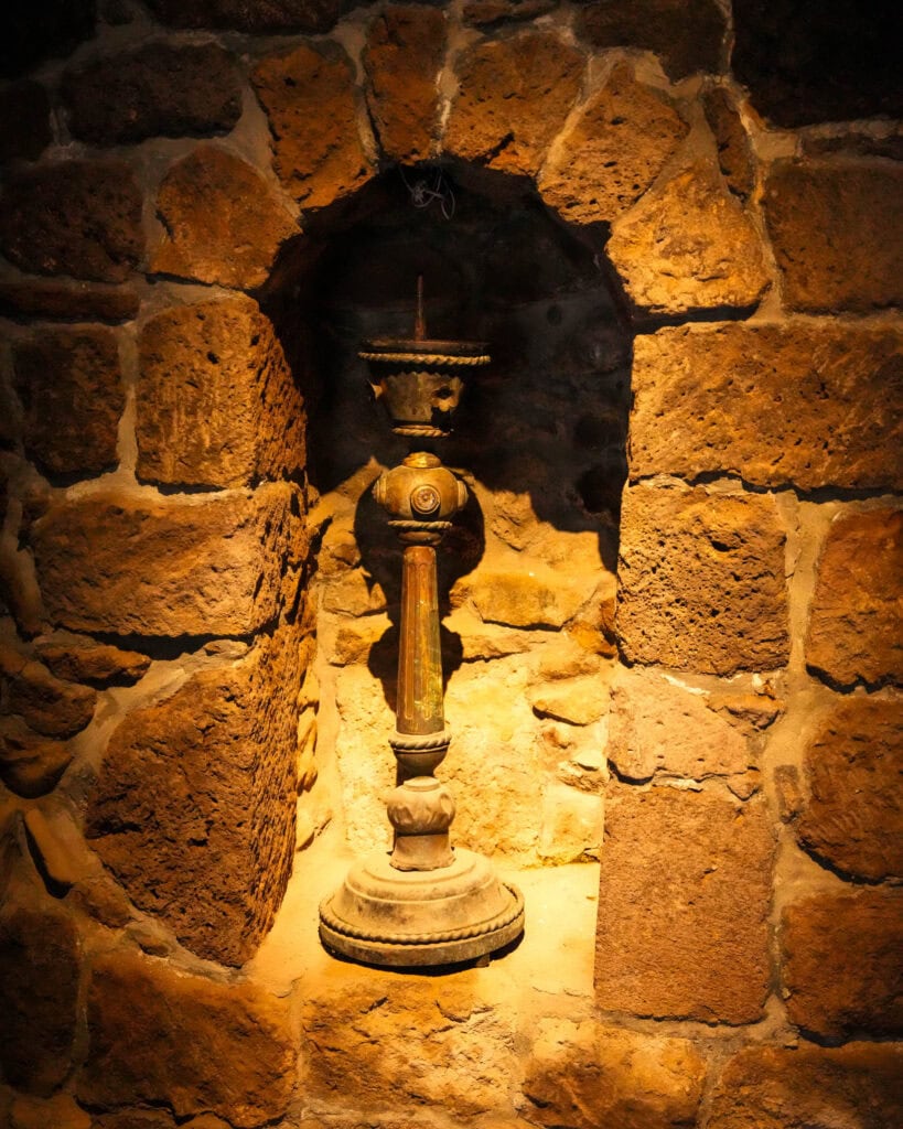 In einer Nische einer Steinmauer steht eine alte Messinglampe, die von warmem Licht erhellt wird.
