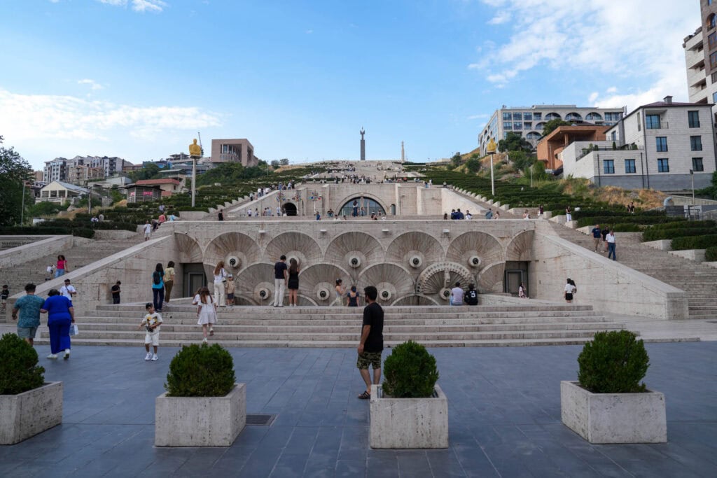 An einem sonnigen Tag spazieren Menschen in der Nähe des Cascade Complex, einer großen Treppe mit Springbrunnen und Grünanlagen.