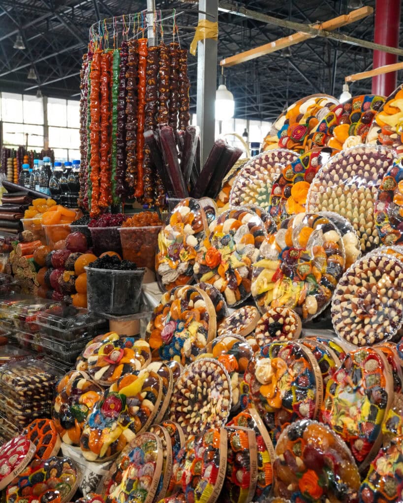 Bunte Arrangements aus Trockenobst und Nüssen, ausgestellt auf einem lebhaften Indoor-Markt mit hängenden Süßigkeiten.
