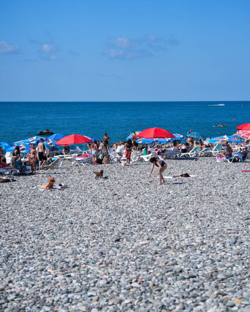 Ein belebter Kieselstrand in Batumi, an dem Menschen am blauen Meer unter bunten Sonnenschirmen sonnenbaden und entspannen.