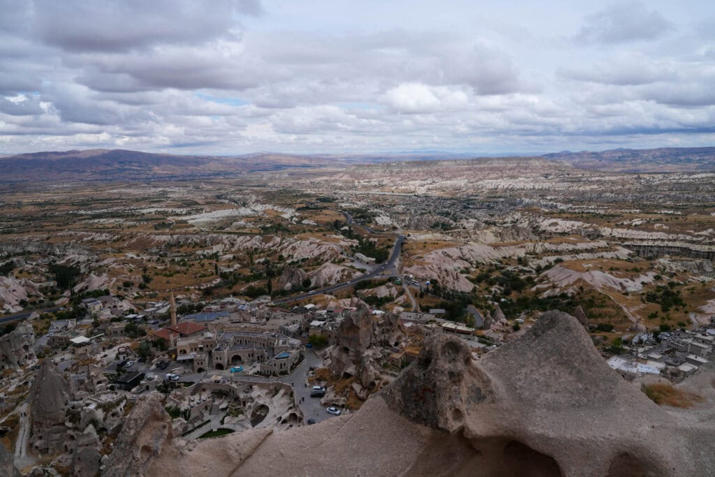 Blick auf eine felsige Landschaft mit vereinzelten Gebäuden, kurvenreichen Straßen und bewölktem Himmel in Kappadokien, Türkei.