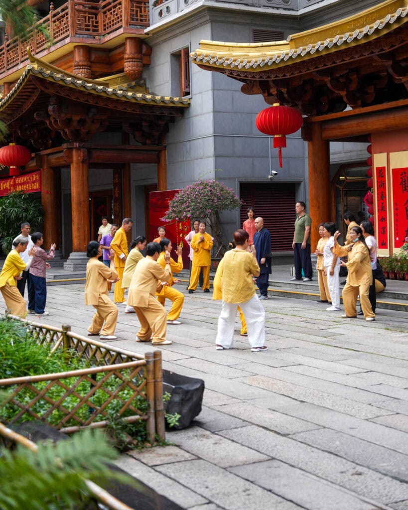Eine Gruppe von Menschen, die in einem Innenhof mit traditioneller chinesischer Architektur Tai Chi praktizieren.