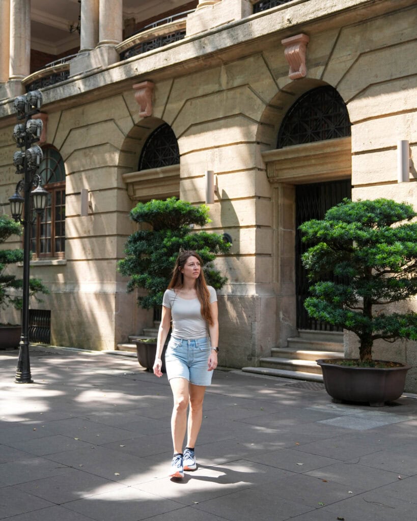 Eine Frau in T-Shirt und Shorts, die auf einem Gehweg vor einem Steingebäude entlanggeht.