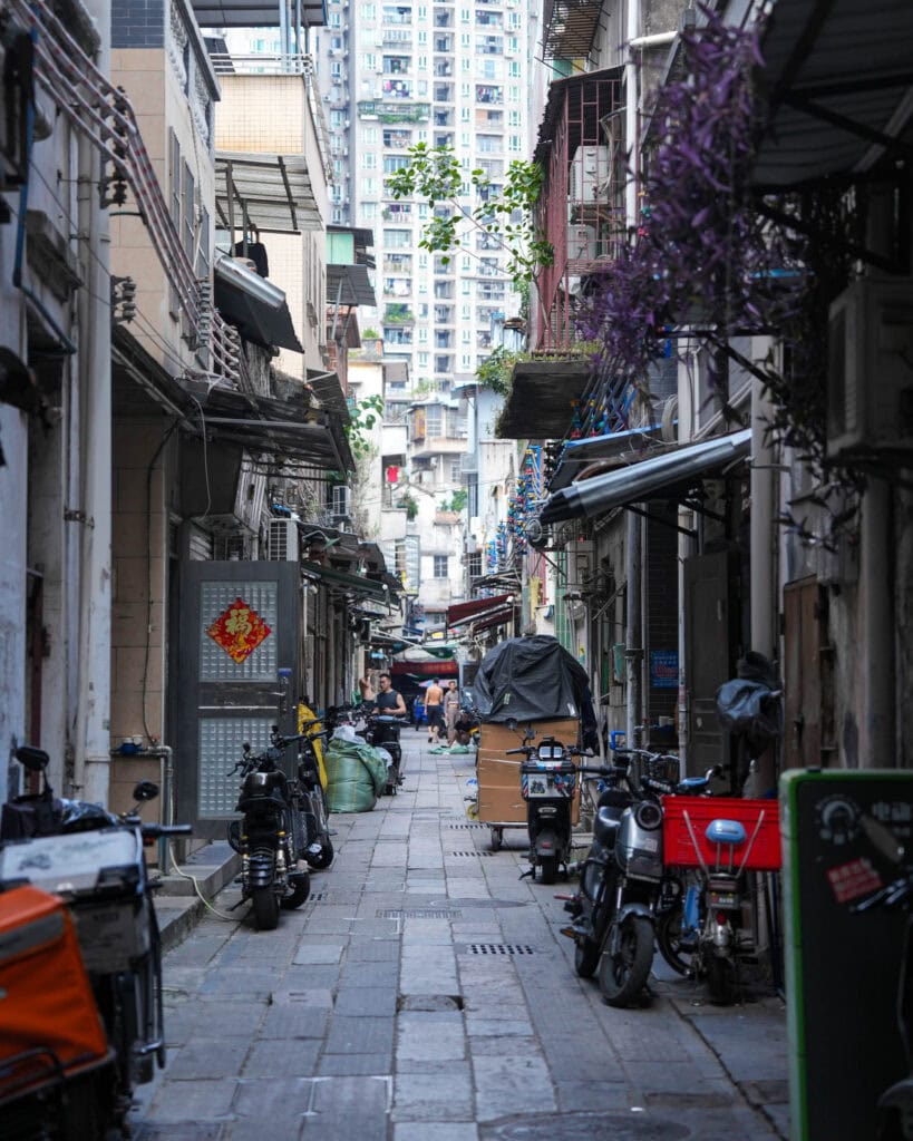 Eine schmale städtische Gasse, gesäumt von geparkten Rollern und Motorrädern.