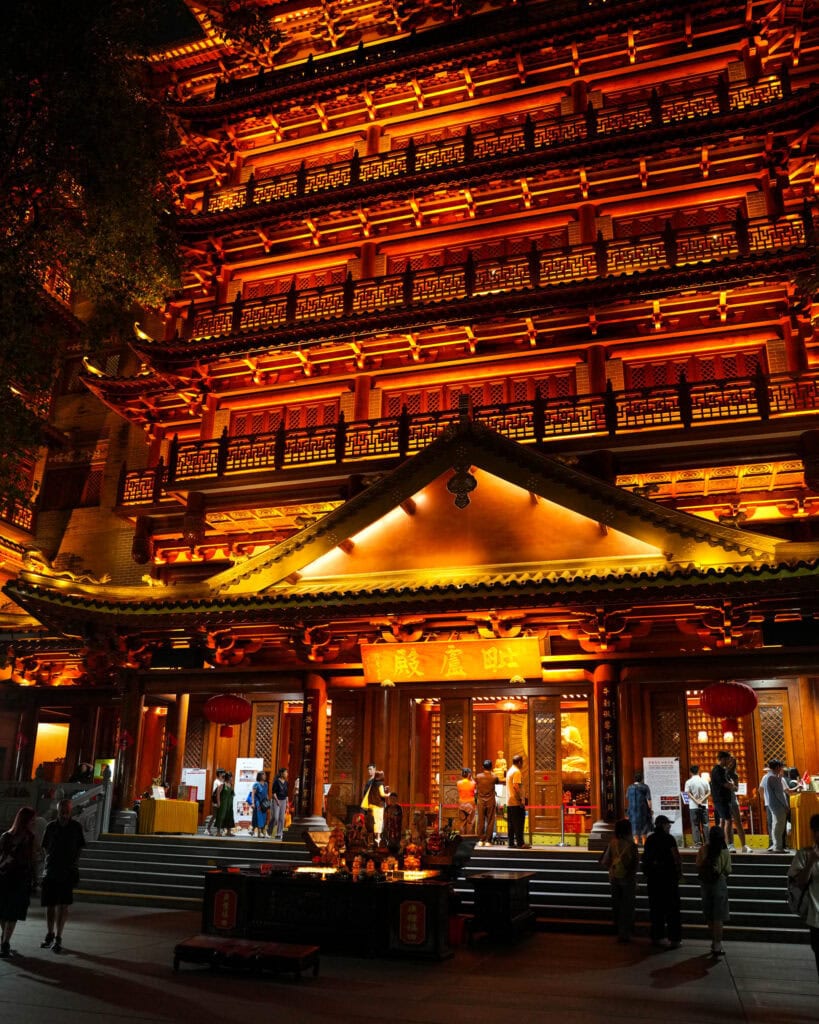 Mehrstöckiger chinesischer Tempel, der nachts beleuchtet ist und über dem Eingang ein Banner hängt.