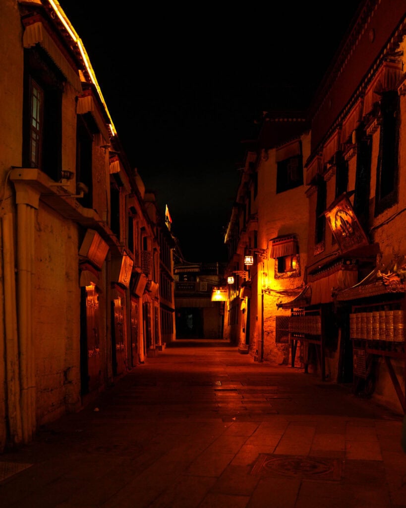 Eine schmale Gasse zwischen traditionellen Gebäuden, die nachts von warmem, goldenem Licht beleuchtet wird.