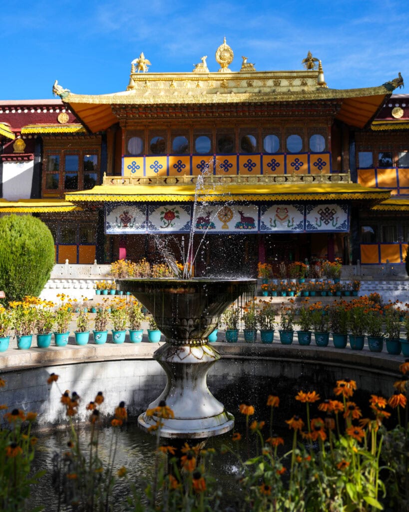 Ein Springbrunnen vor einem kunstvoll verzierten Tempel mit goldenem Dach.